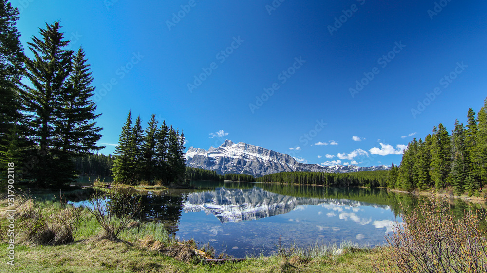 Obraz premium Early morning view from Two Jack Lake in Rocky mountains Canada Alberta Rockies with mountain reflecting mirror in water with blue skies 