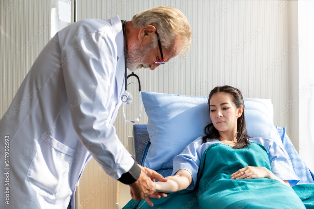 Obraz premium Senior Caucasian doctor man reassuring and discussing Asian patient woman in the hospital room.