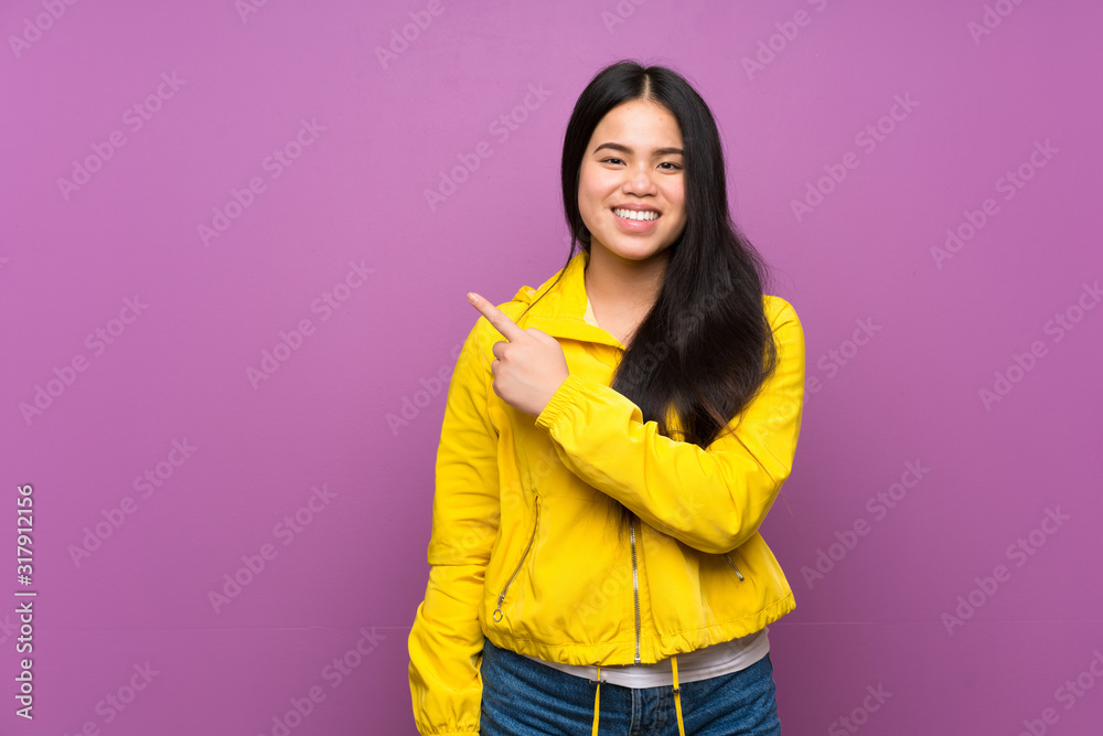 Young teenager Asian girl over isolated purple background pointing to the side to present a product Young teenager Asian girl over isolated purple background pointing to the side to present a product