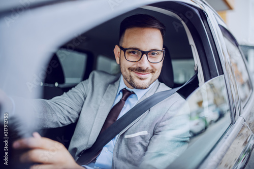 Attractive caucasian smiling elegant unshaven businessman in suit and eyeglasses driving his expensive car.