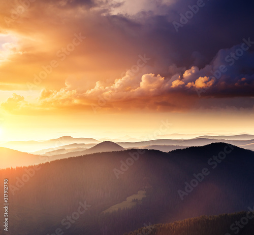 Alpine mountains are illuminated by the sunset. Picture of colorful cloudy sky.