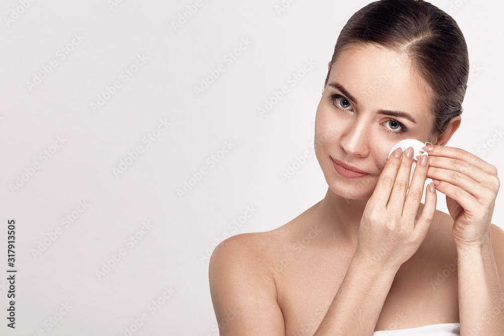 Healthy fresh girl removing makeup from her face with cotton pad. Beauty woman cleaning her face with cotton swab pad isolated on grey background. Skin care and beauty concept. Healthy fresh girl removing makeup from her face with cotton pad. Beauty woman cleaning her face with cotton swab pad isolated on grey background. Skin care and beauty concept.