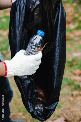 Close up hand young volunteers man keep bottle plastic put in garbage bags cleaning area in park, Reduce plastic, reduce global warming.