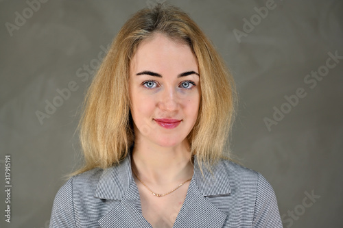 Portrait of a pretty cute smiling young blonde business woman with minimal makeup in a gray suit on a gray background. It stands directly opposite the camera in various poses.