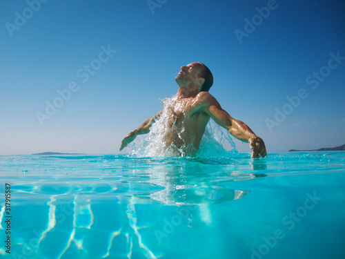 Athletic man emerging with a splash from rippling blue water