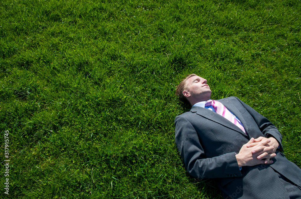 Relaxed businessman lying on a bright green grass field on a sunny spring day Relaxed businessman lying on a bright green grass field on a sunny spring day