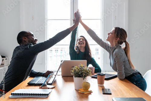 Group of successful young businesspeople holding up their right hands on coworking place. photo