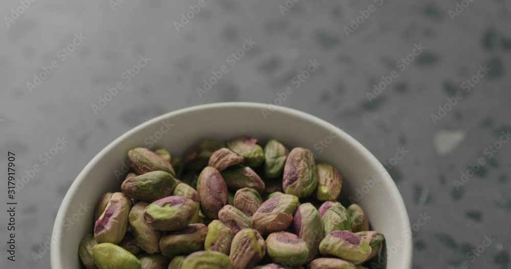 Handheld slow motion peeled pistachios in white bowl on terrazzo surface Handheld slow motion peeled pistachios in white bowl on terrazzo surface