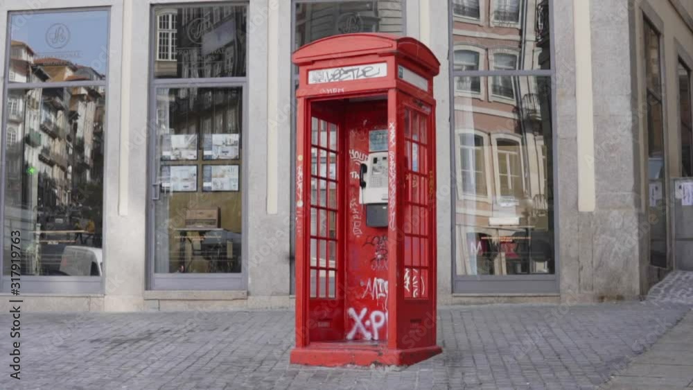 Interesting old-fashioned red telephone box on the roadside in Porto, Portugal, located near old city, cafe on the background, outdoor, static shooting. Interesting old-fashioned red telephone box on the roadside in Porto, Portugal, located near old city, cafe on the background, outdoor, static shooting.