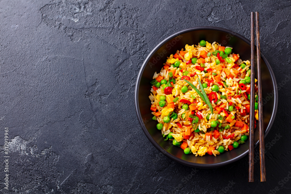 Asian fried rice with egg and vegetables. Black background. Cope space. Top view.