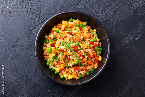 Asian fried rice with egg and vegetables. Dark stone background. Top view.