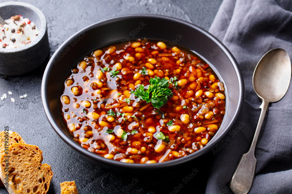 Bean soup in a black bowl. Dark background. Close up. Bean soup in a black bowl. Dark background. Close up.