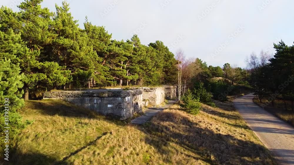 Aerial view of concrete Northern fortification ruins covered by green vegetation and trees located in Liepaja, Latvia in sunny day, wide angle establishing drone shot moving forward Aerial view of concrete Northern fortification ruins covered by green vegetation and trees located in Liepaja, Latvia in sunny day, wide angle establishing drone shot moving forward