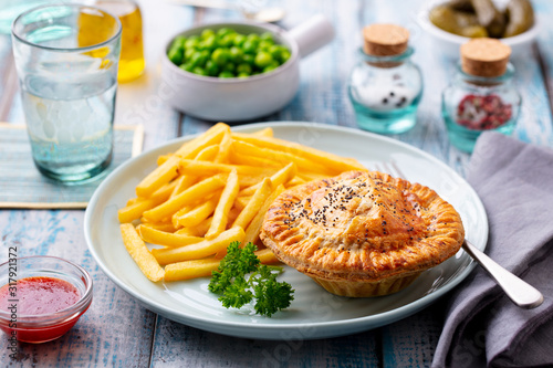 Meat pie with french fries on a white plate. Wooden background. Close up.