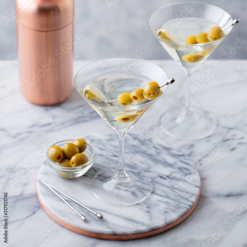 Martini cocktail with olives and bar shaker on marble table background.