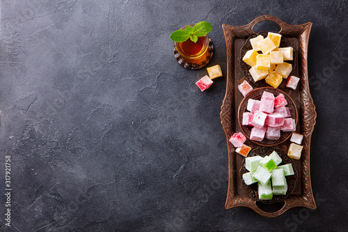 Assortment of Turkish delights on a authentic tray with glass of tea. Dark background. Top view. Copy space.