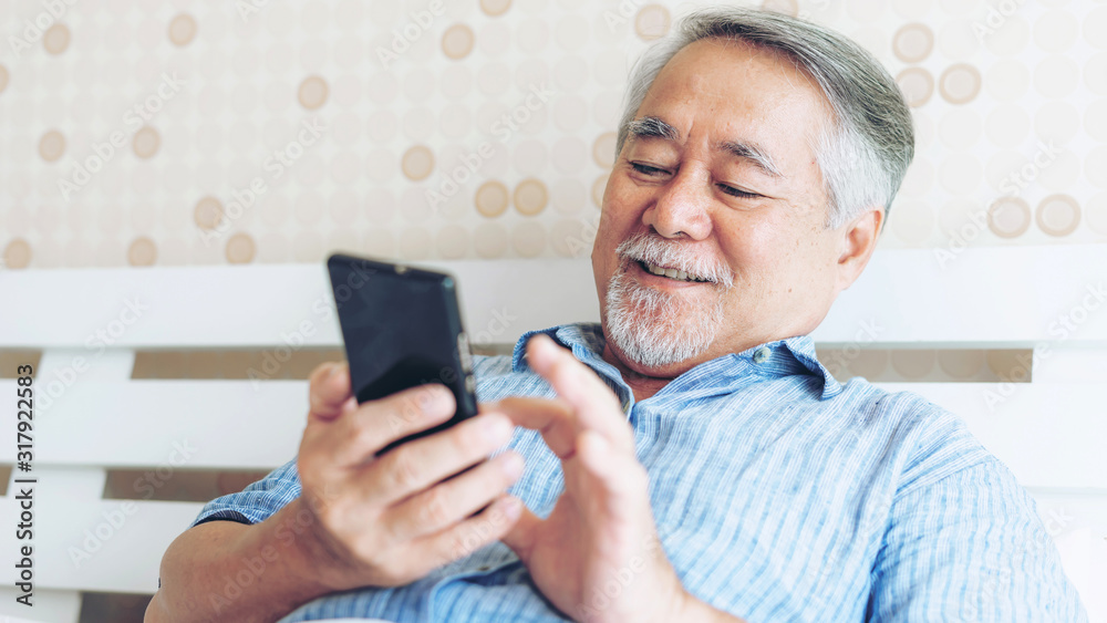 Senior Male using a smartphone , smiling feel happy in bed at home - lifestyle senior concept Senior Male using a smartphone , smiling feel happy in bed at home - lifestyle senior concept