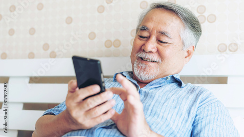 Senior Male using a smartphone , smiling feel happy in bed at home - lifestyle senior concept