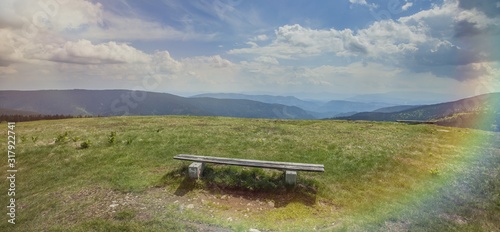 Panoramic shot of a wooden bench in the field in Slovenia with a rainbow on the right corner photo