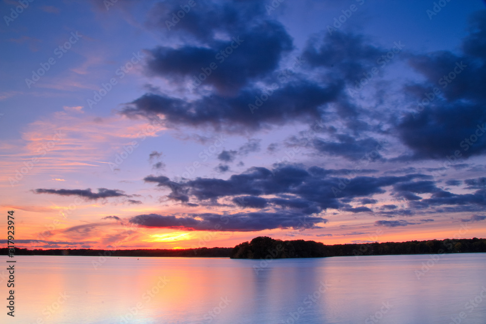 View of the lake at sunset with picturesque play of colors, silhouettes and a peaceful atmosphere.