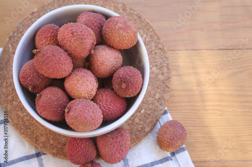 Fresh ripe litchi or lychee fruits in a bowl on wooden background. Litchi chinensis fruit on table