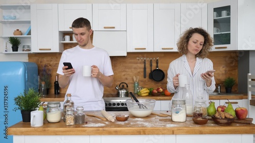 Young Couple Using Cell Phones On Kitchen. Obsession With Technology.