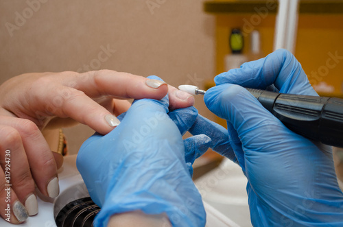 Hardware manicure procedure. Master in blue gloves removes gel polish from nails with a white cutter