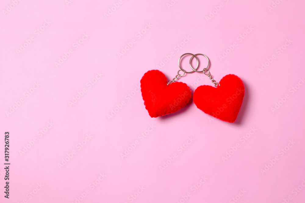 Two hearts on the car keychain. Two red hearts placed on a pink background. Two heart shaped key chains tied together.