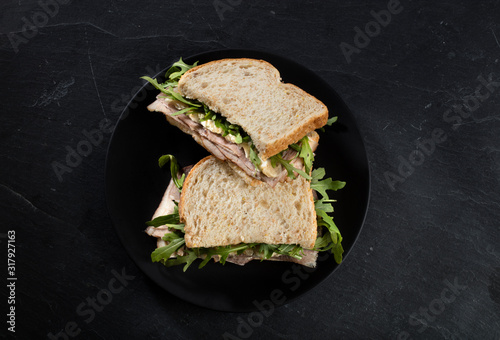 sandwich  integral de jamón queso y rucula sobre fondo negro. Sándwich integral de jamón, queso y rúcula sobre fondo negro. photo