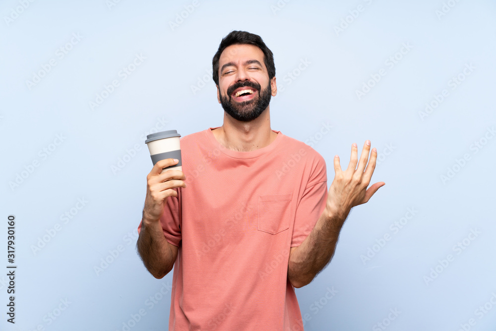 Young man with beard holding a take away coffee over isolated blue background smiling a lot Young man with beard holding a take away coffee over isolated blue background smiling a lot