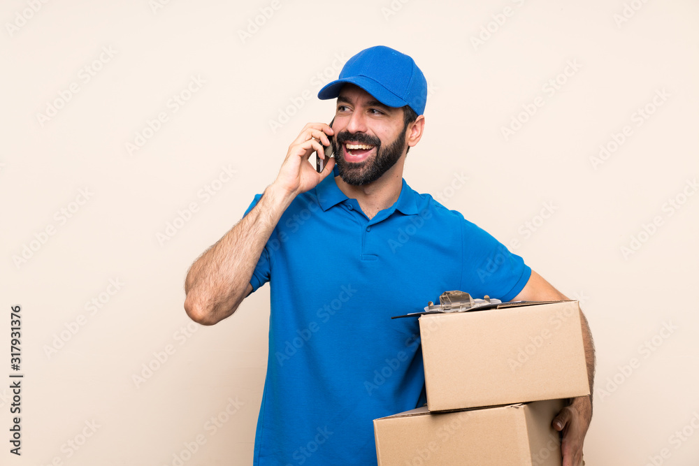Delivery man with beard over isolated background keeping a conversation with the mobile phone Delivery man with beard over isolated background keeping a conversation with the mobile phone