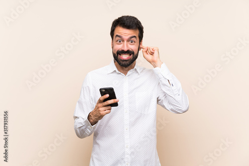 Young man with beard holding a mobile frustrated and covering ears © luismolinero