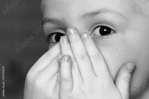 Close-up portrait of a little boy with hands on mouth, black and white
