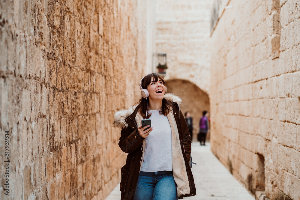 .Young female tourist visiting Mdina, former capital of Malta. Listening to music in a relaxed way while touring the ancient city, smiling and carefree. Lifestyle