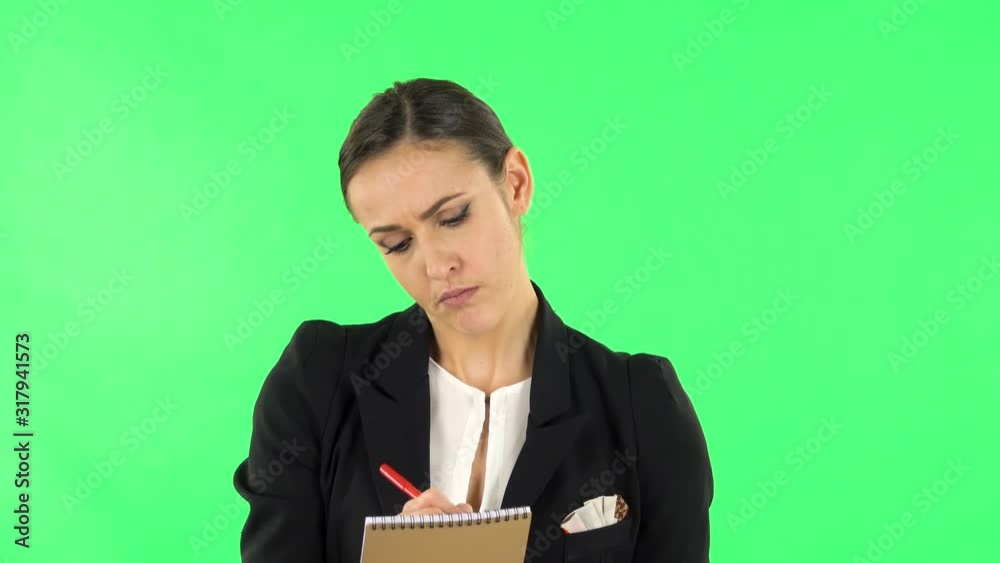Girl stands and thinks, then angrily writes with pencil in notebook. Green screen