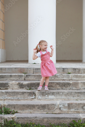 A small cute girl in a pink dress girl on on the stone steps on a Sunny day. Selective focus © fieryphoenix