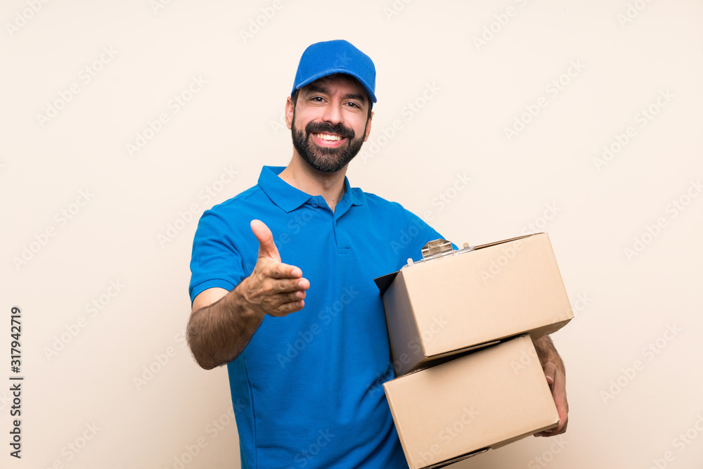 Delivery man with beard over isolated background shaking hands for closing a good deal Delivery man with beard over isolated background shaking hands for closing a good deal