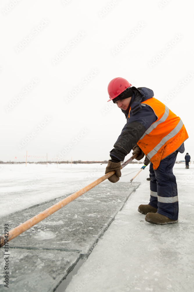 Worker rafts ice blocks along a canal carved in a frozen lake