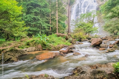 view of stream silky water flowing around with arch rocks, green forest and waterfalls background, Khlong Lan Waterfalls, Khlong Lan National Park, Kamphaeng Phet, Thailand.
