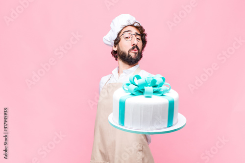 young crazy baker man holding a cake against pink wall photo