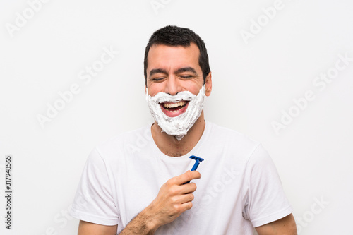 Man shaving his beard over isolated white background smiling a lot