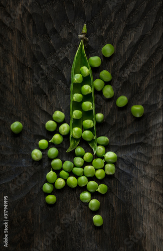 Open Pod and the scattered fresh green peas on a dark wooden background