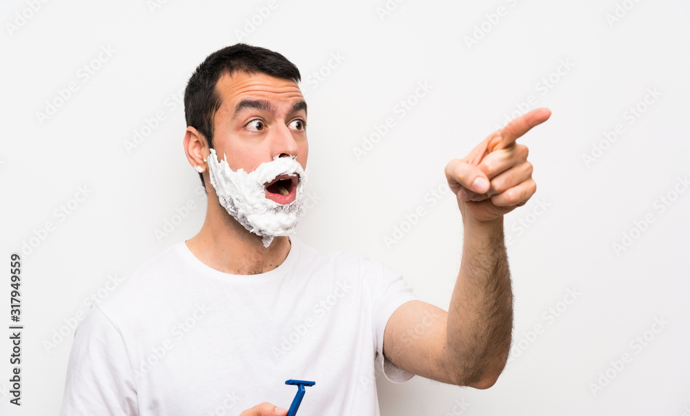 Man shaving his beard over isolated white background pointing away