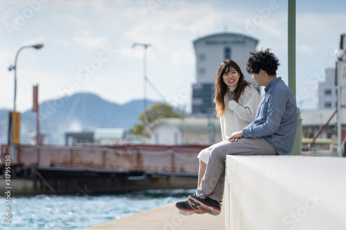 堤防に腰掛け楽しそうに会話をする若いカプル © west_photo