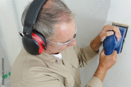 builder in hardhat sanding wall indoors photo