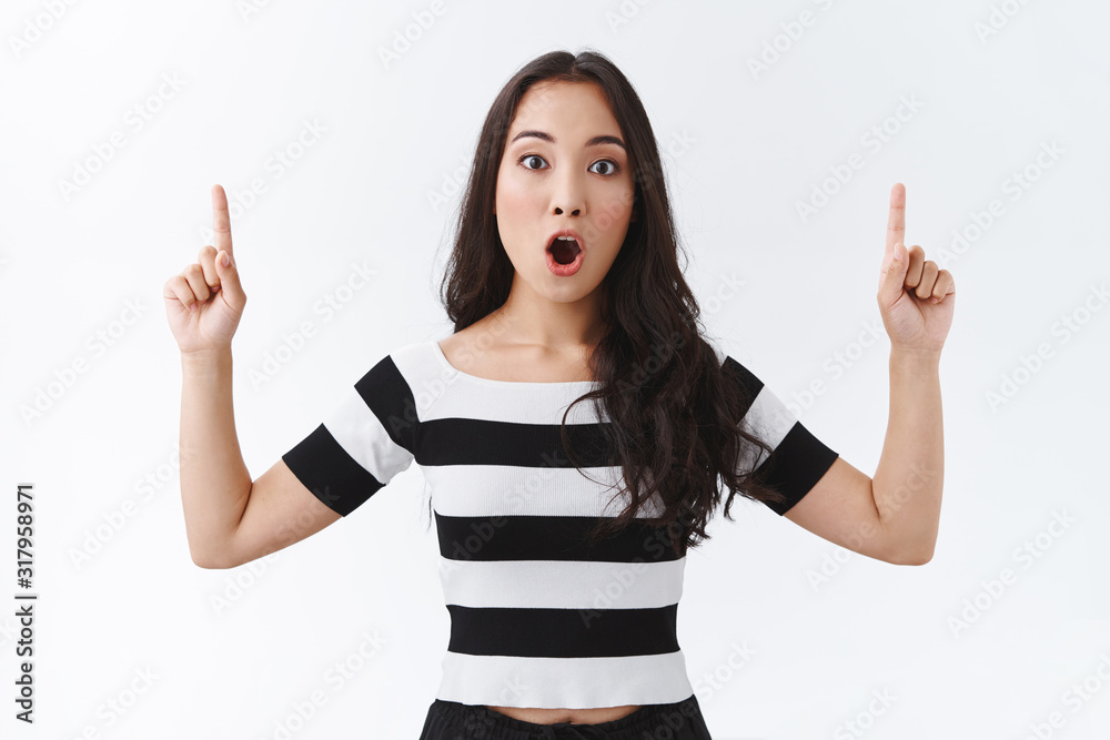 Astonishment and emotions concept. Portrait of attractive brunette asian woman in striped t-shirt, gasping drop jaw impressed, stare camera impressed, raise fingers pointing up, white background Astonishment and emotions concept. Portrait of attractive brunette asian woman in striped t-shirt, gasping drop jaw impressed, stare camera impressed, raise fingers pointing up, white background