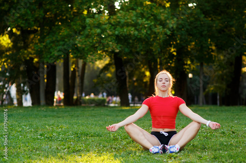 Young beautiful woman doing yoga sitting on the grass in the Park. training and stretching muscles in nature