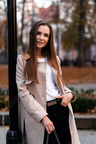 Outdoor fashion portrait of stylish young woman having fun, emotional face , laughing, Urban city street style wearing dark casual trousers, white sweater,creamy coat. and sunglasses Fashion concept.