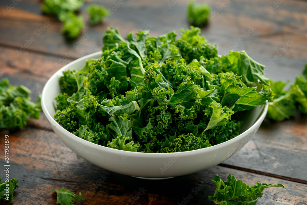 Raw Organic Kale in white bowl on wooden table Raw Organic Kale in white bowl on wooden table