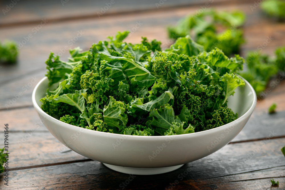 Raw Organic Kale in white bowl on wooden table Raw Organic Kale in white bowl on wooden table